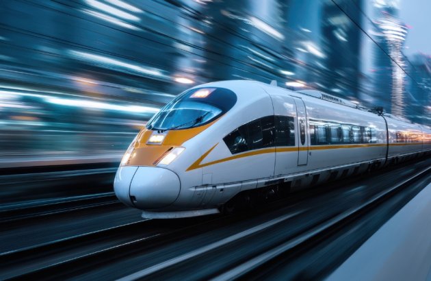 Mobilität-Ein eleganter Hochgeschwindigkeitszug rast an der in der Abenddämmerung beleuchteten Skyline einer Stadt vorbei. Die schimmernden Lichter und die schnelle Bewegung unterstreichen die fortschrittliche Technologie und