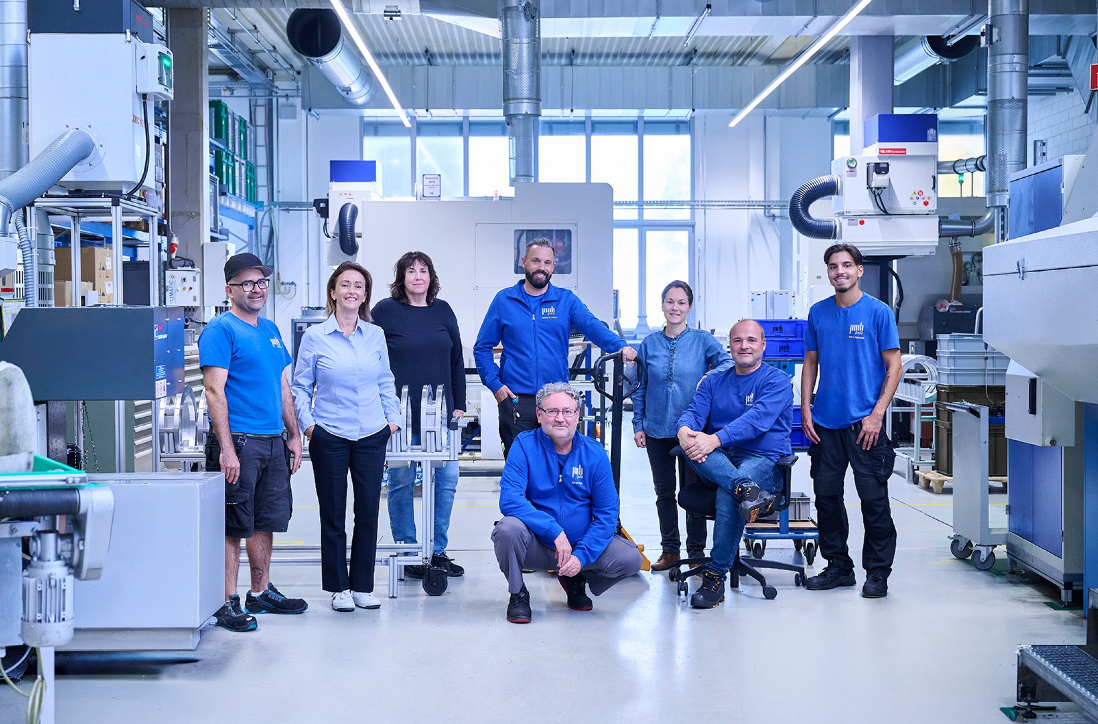 Mehrere Personen stehen in einer Produktionshalle für mechanische Fertigungsteile im Hintergrund sind CNC Maschinen zu sehen