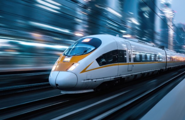 Mobilität-Ein eleganter Hochgeschwindigkeitszug rast an der in der Abenddämmerung beleuchteten Skyline einer Stadt vorbei. Die schimmernden Lichter und die schnelle Bewegung unterstreichen die fortschrittliche Technologie und